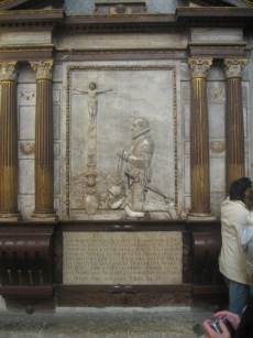A stone relief of a man kneeling in front of a cross